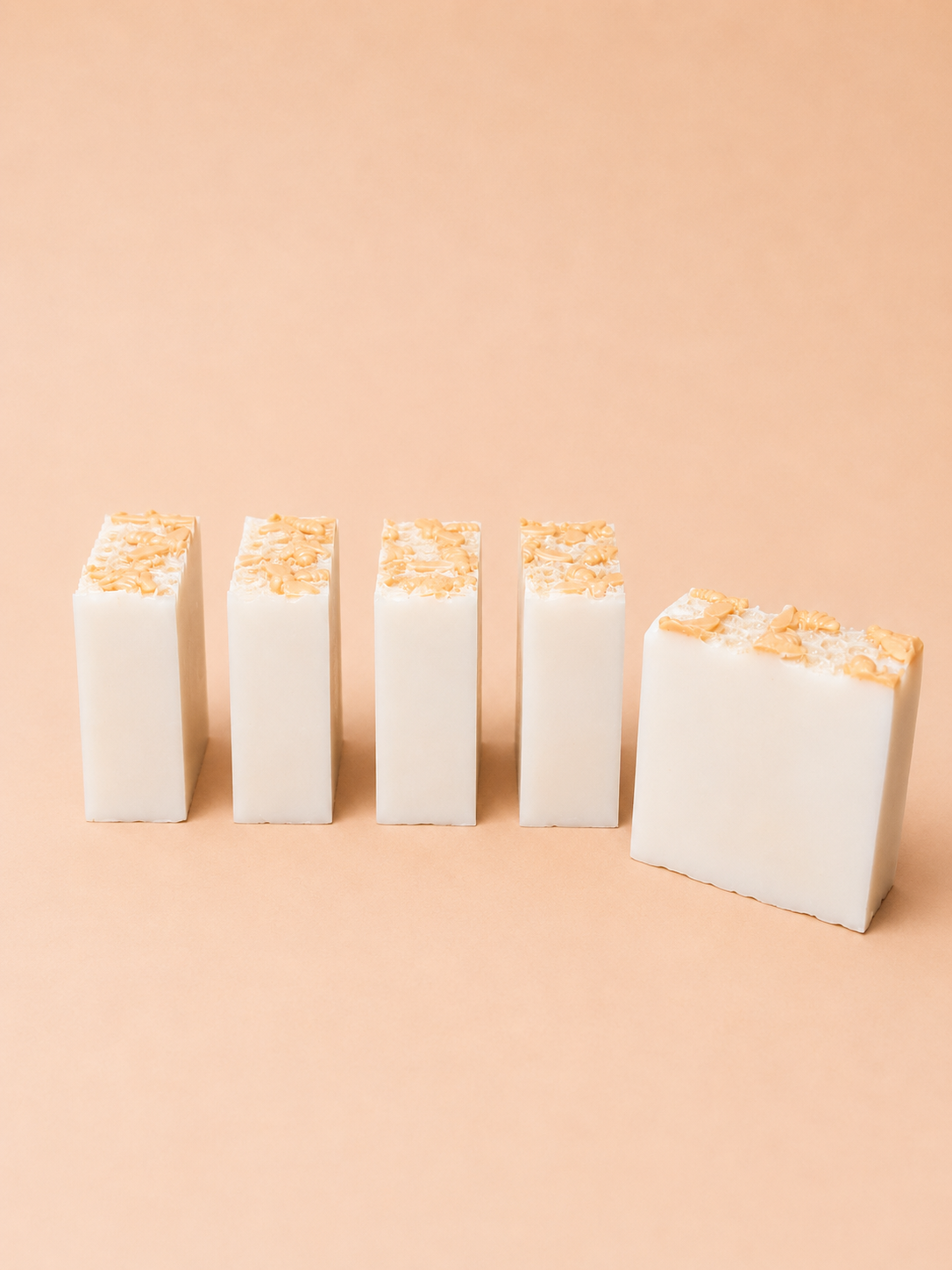 Five white bars of soap with gold accents arranged in a row on a beige background